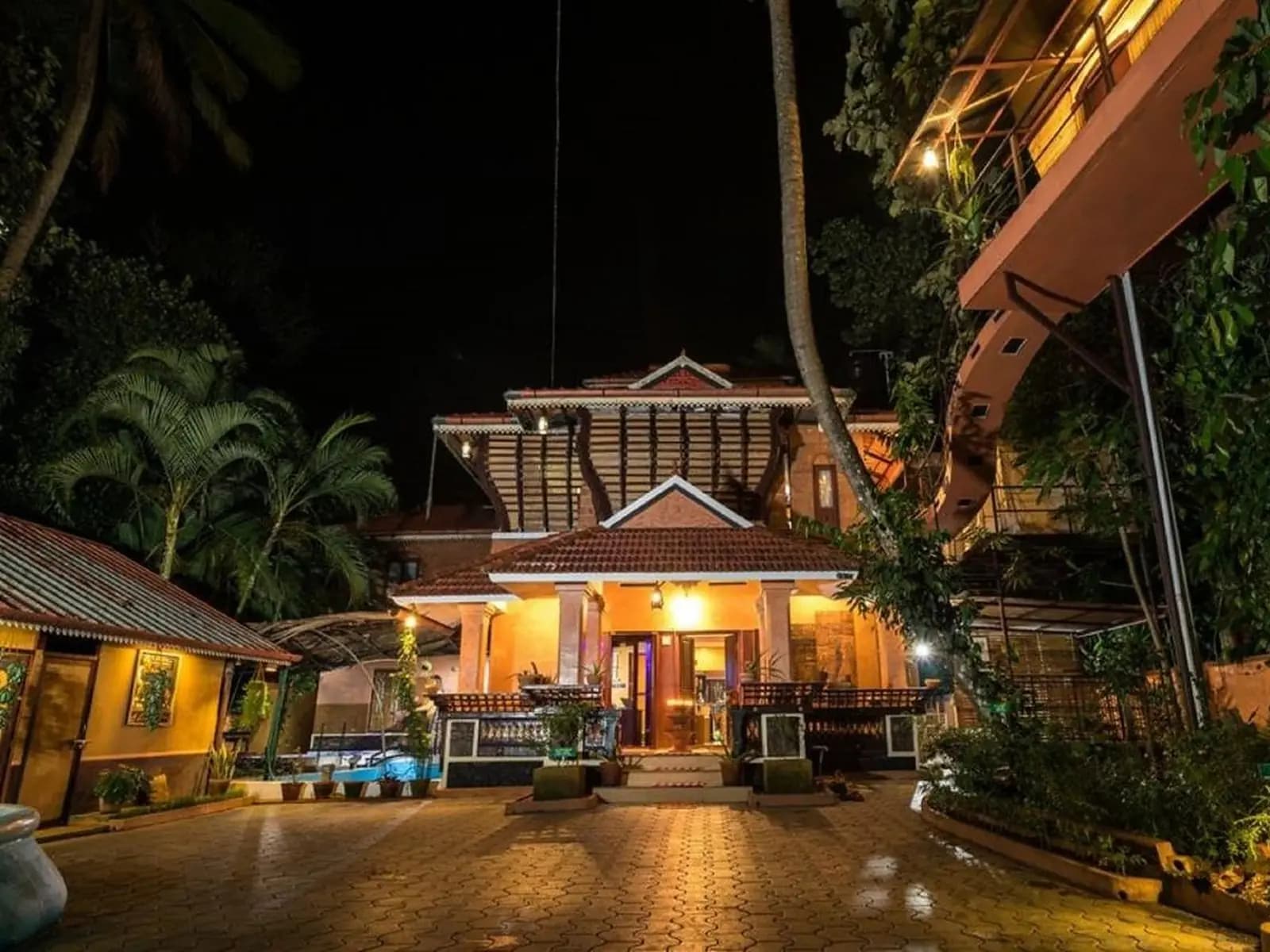 Lit Kerala-style house among palms at night at an Ayurveda retreat by the Kuttampuzha River