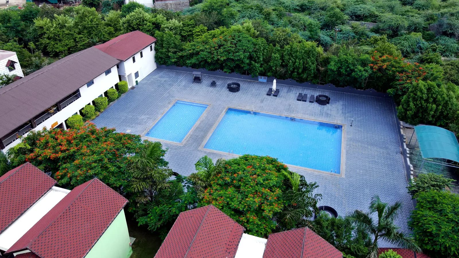 Two outdoor pools on a paved deck surrounded by gardens and cottages at a resort in Abu Road, Rajasthan