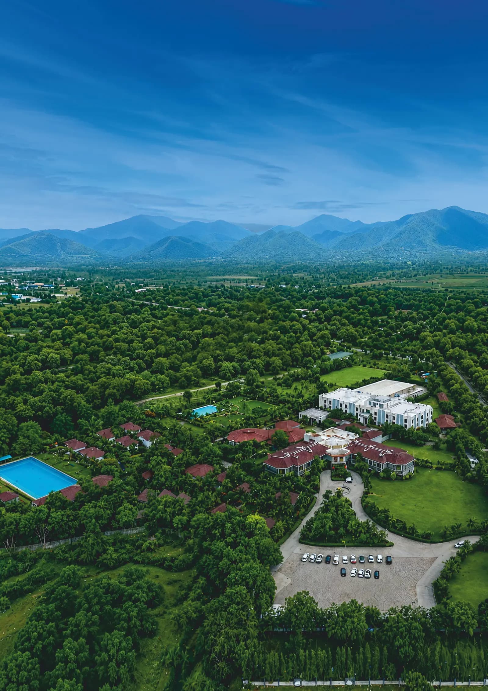 Aerial view of a green resort campus with a pool below the hills of Mount Abu, Rajasthan