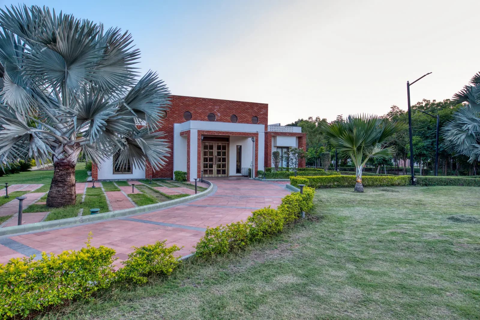 Curved brick path through a garden with palms to a pavilion at a Naturopathy centre in Gujarat