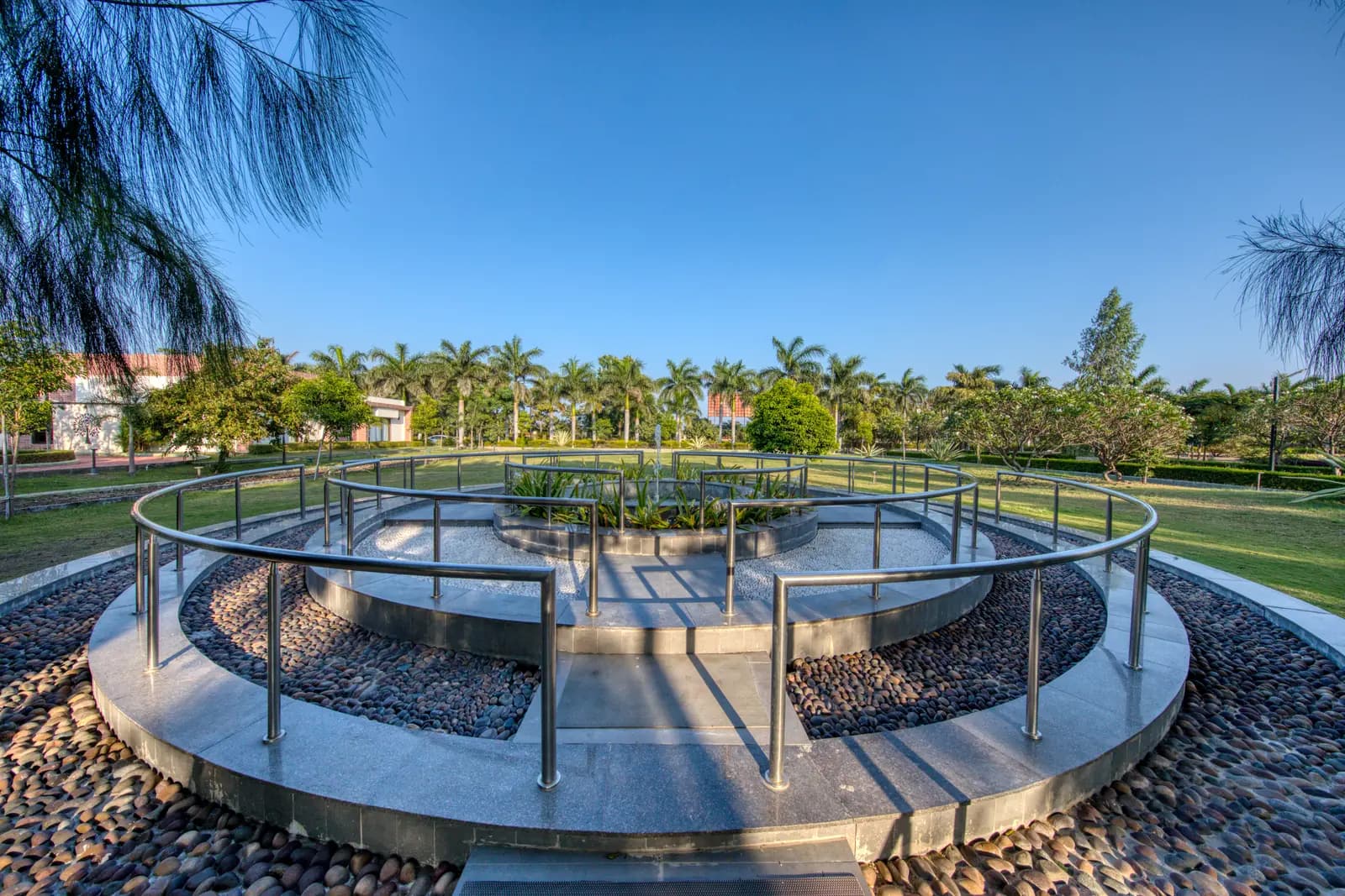 Curved brick path through a garden with palms to a pavilion at a Naturopathy centre in Gujarat