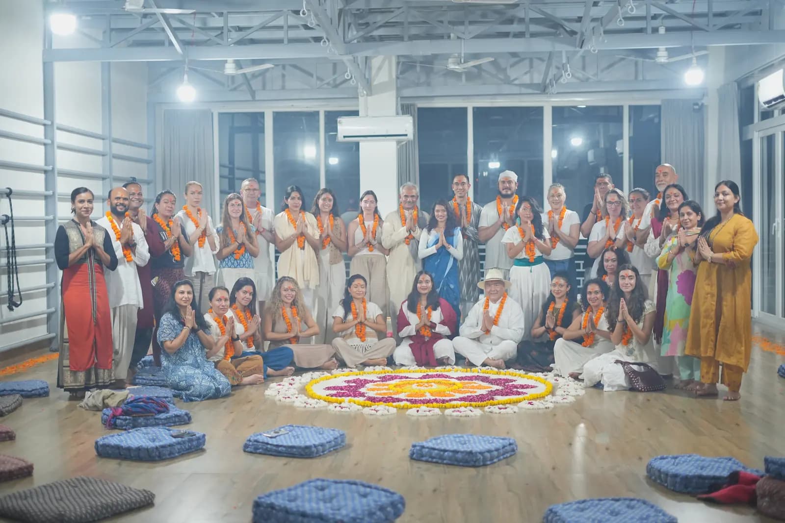 Yoga teacher training graduates in garlands around a flower rangoli in a yoga hall in Rishikesh
