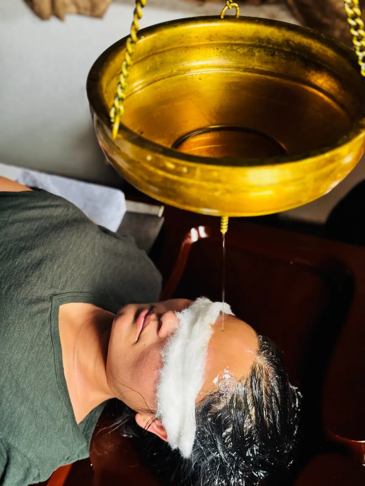 Shirodhara therapy with warm oil poured from a brass vessel onto a guest's forehead in Rishikesh