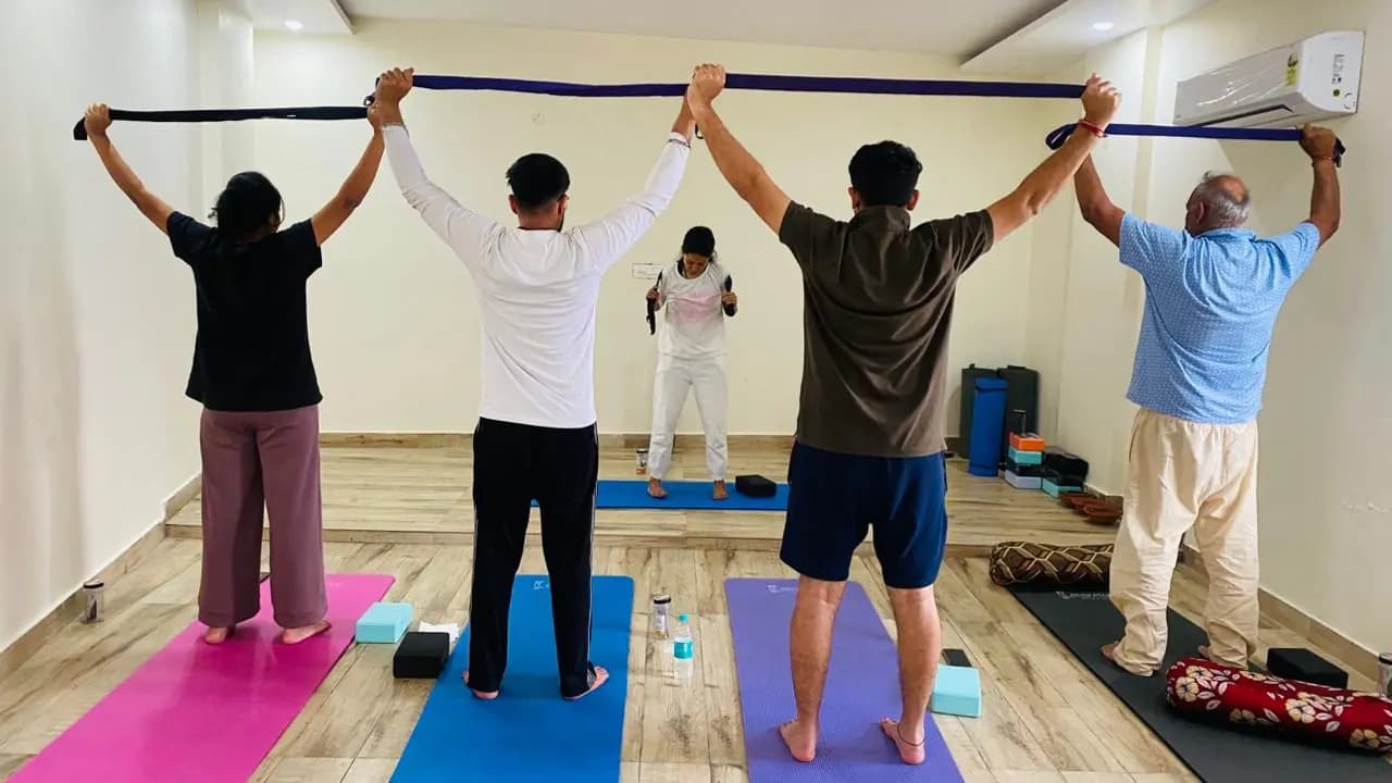 Small group stretching with yoga straps overhead in an indoor yoga hall in Rishikesh