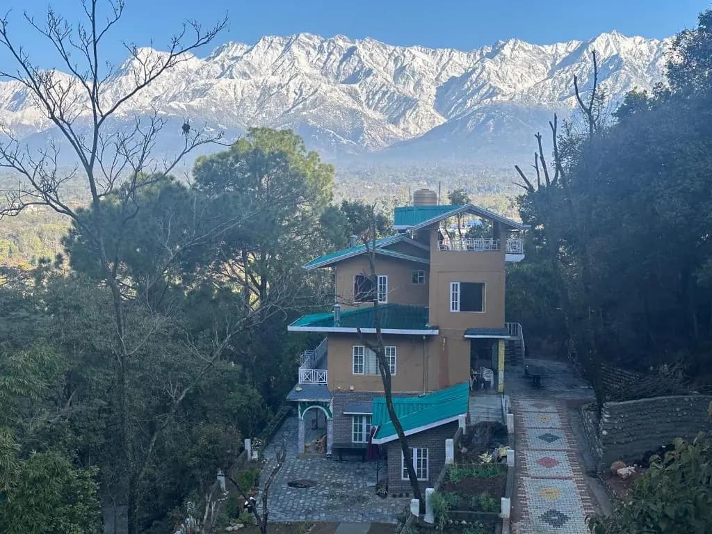 Guesthouse on a forested hillside facing the snowy Dhauladhar range near Palampur, Himachal Pradesh